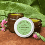 Comfrey Magic Skin and Bone Salve by My Herbal Apothecary in amber jars, with comfrey leaves and pink comfrey flowers in the background.