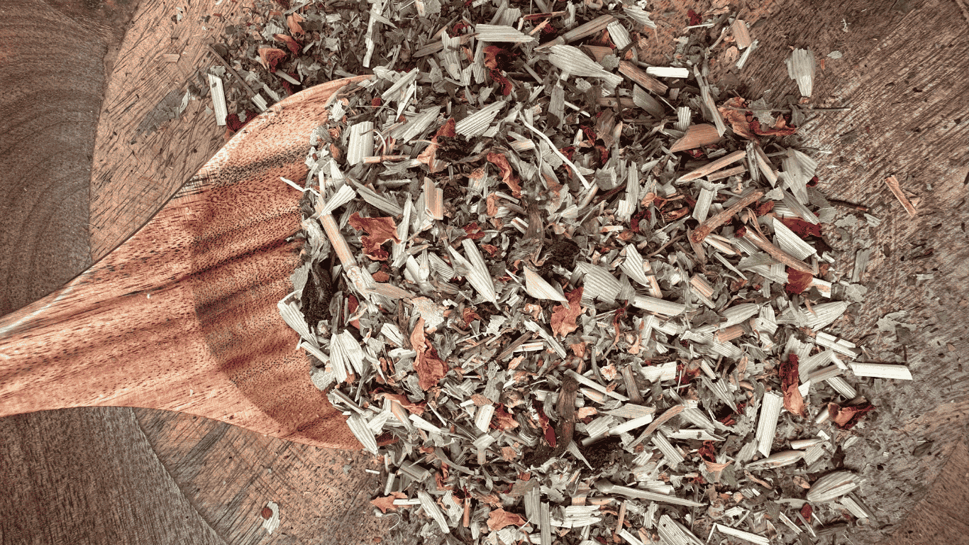 A close-up of loose dried herbs from the Sorrow Organic Herbal Tea Blend, featuring vibrant oat straw, rose petals, lemon balm, butterfly pea flowers, and other botanicals on a wooden spoon and bowl.