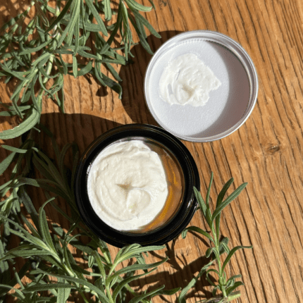 An open jar of Whip Dreams Tallow Balm from My Herbal Apothecary, sitting on a warm wooden surface with fresh lavender sprigs nearby. The creamy, whipped texture of the balm is clearly visible inside the dark amber jar, with a small amount also shown on the inside of the lid. A natural, Australian-made skincare product featuring grass-fed beef tallow and essential oils.