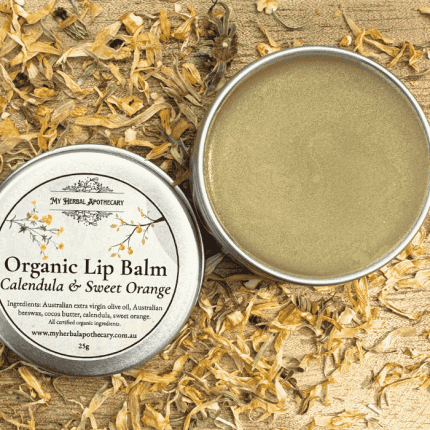 Tin of Organic Lip Balm – Calendula & Sweet Orange from My Herbal Apothecary, shown open and closed, surrounded by dried calendula petals on a rustic wooden background. The label lists all certified organic ingredients and features delicate botanical artwork.