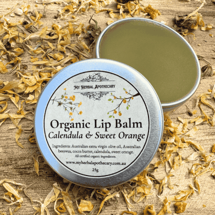 Tin of Organic Lip Balm – Calendula & Sweet Orange from My Herbal Apothecary, shown open and closed, surrounded by dried calendula petals on a rustic wooden background. The label lists all certified organic ingredients and features delicate botanical artwork.