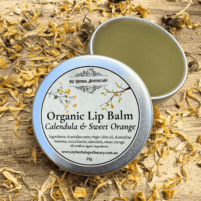 Tin of Organic Lip Balm – Calendula & Sweet Orange from My Herbal Apothecary, shown open and closed, surrounded by dried calendula petals on a rustic wooden background. The label lists all certified organic ingredients and features delicate botanical artwork.