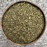 Organic spearmint dried leaf sitting in a coconut bowl on a stone background.