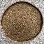 Organic dried Tulsi Holy Basil leaves sitting in a coconut bowl with a stone background.